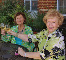 two women are drinking wine at an outdoor table