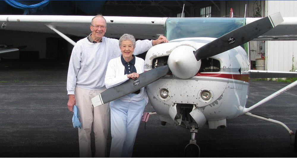 an elderly man and woman standing in front of a plane